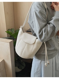 Close-up of white bucket bag featuring pebble leather texture and golden metal detailing