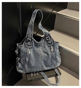 Detail of blue washed denim tote bag showing decorative zippers and heavy fabric texture