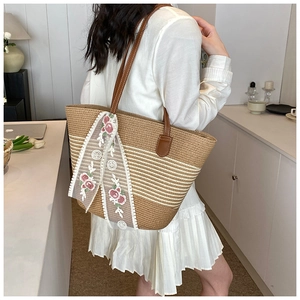 Detail of woven straw tote bag featuring white lace bow and pink floral embroidery