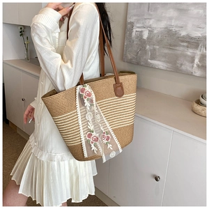 Detail of hand-woven straw tote bag with pink floral lace ribbon and brown leather handle