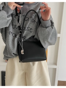 Model wearing black faux leather shoulder bag with a silver crescent charm detail