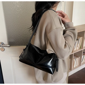 Detail view of a black glossy underarm bag with silver zipper worn by a model