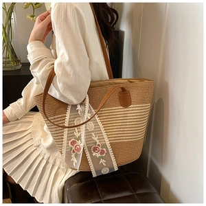 Detail view of woven straw tote bag featuring brown leather straps and pink rose lace scarf