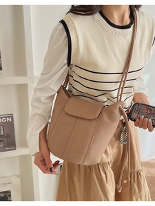 Close-up of beige lychee leather bucket bag with drawstring and metal accents