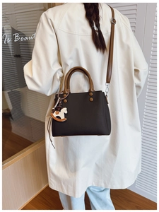 Detail of minimalist black and brown crossbody bag with white wooden horse charm accessory
