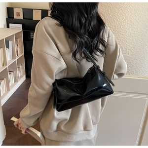 Detail of glossy black patent leather shoulder bag with adjustable strap and zipper
