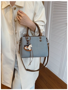 Detail view of a light blue canvas crossbody bag with brown leather straps and a horse charm