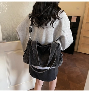Washed black denim tote bag shown worn on shoulder to display large capacity and style