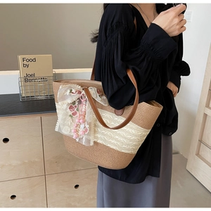 Detail der gewebten Strohtasche mit braunen Lederriemen und floralem Spitzenbogen-Anhänger