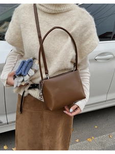 Detail of a dark brown leather underarm bag with a stylish metal chain strap decoration