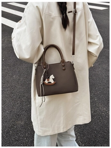 Detail view of dark coffee tote bag with litchi texture and cute horse charm on model