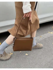 Detail of a dark brown matte leather underarm bag featuring a stylish silver chain accent