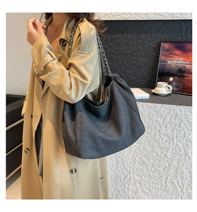 Detail of grey denim tote bag with silver chain strap shown on model in modern office setting