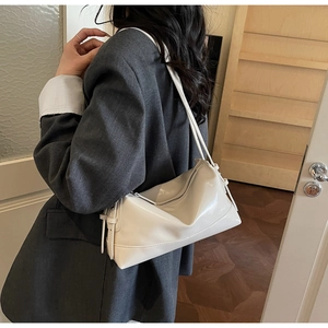 Chic white glossy shoulder bag with asymmetric folding shown on a model in home setting