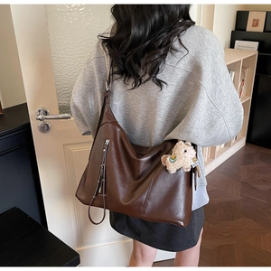 Détail du sac hobo en cuir marron foncé avec fermeture éclair et pendentif agneau peluche