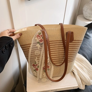 Close-up of woven straw tote bag featuring embroidered lace ribbon and leather handles