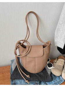 Detailed view of light brown leather bucket bag on denim and knitwear lifestyle setting
