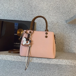 Detail of light pink crossbody bag with brown handles and a stylish horse charm accessory