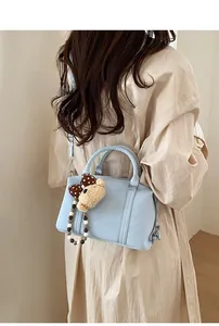 Close-up of light blue Boston bag with embossed lettering and a cute bear charm pendant