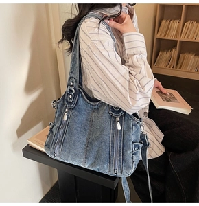 Detail of vintage washed blue denim shoulder bag featuring zippers and distressed texture