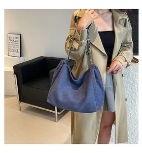 Detail of blue denim tote bag featuring silver chain strap worn with khaki trench coat