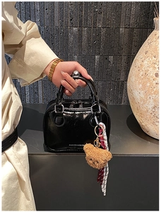 Détail du sac à main en cuir verni noir avec zips argentés et breloque ours
