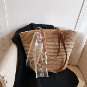 Close-up of woven straw tote bag featuring brown leather handles and floral lace scarf detail