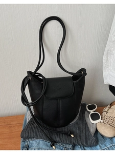 Detail view of black lychee texture bucket bag with thin rope straps on a wooden table