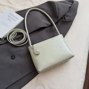 Detail of minimalist beige underarm bag with silver fashion charm on a grey blazer
