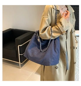 Detail of dark blue denim tote bag with silver chain strap worn by a model in a trench coat