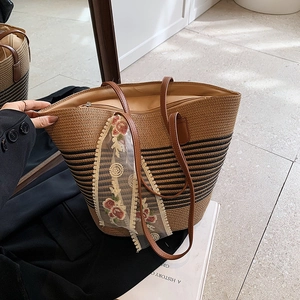Detail of straw tote bag with black stripes, brown leather handles and floral lace scarf