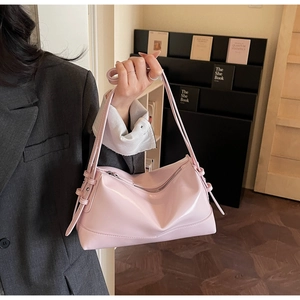 Detail of a light pink glossy leather underarm bag with decorative side straps and metal buckles