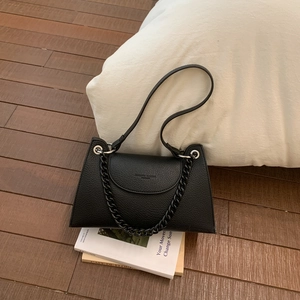 Detail of black lychee grain leather handbag featuring structural trapezoid shape and chain