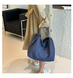 Detail of blue denim tote bag featuring metal chain strap and pleated closure design