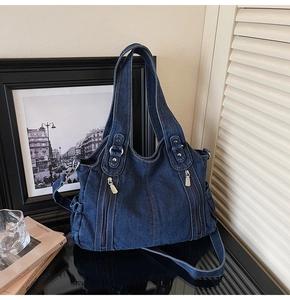 Detailed macro view of dark blue denim fabric texture and silver zippers on a shoulder bag