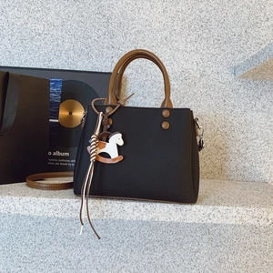 Close-up of black crossbody bag with brown round handle and wooden horse charm detail