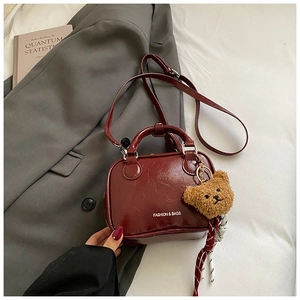 Détail du sac bandoulière en cuir verni bordeaux foncé avec breloque ours et logo fashion