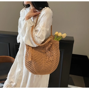 Close-up of hollow crochet straw tote bag with woven strap and large decorative tassel
