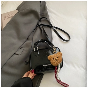 Détail du mini sac noir en cuir verni avec breloque ours en peluche sur blazer gris