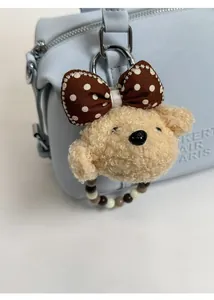 Close-up of cute plush puppy charm with brown polka dot bow on a blue Boston bag