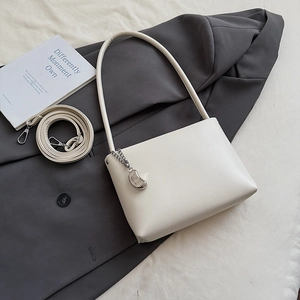 Detailed view of beige underarm bag with silver metal pendant on dark blazer background