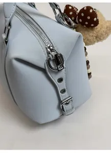 Close-up of light blue Boston bag featuring soft leather, metal zippers and plush bear charm