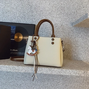 Detail of off-white canvas and brown leather handbag with horse charm on a stone display