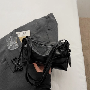 Detail of black glossy handbag with top handles and adjustable long shoulder strap
