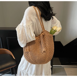 Detail of handwoven straw tote with fringe tassels on a white lace dress backdrop