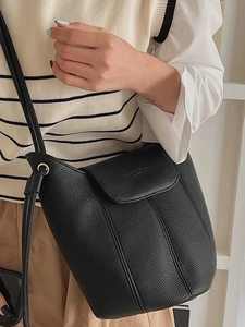Minimalist black pebbled leather bucket bag with top flap and slim shoulder strap