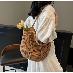 Detail view of brown woven straw shoulder bag with hollow mesh design and long side tassels