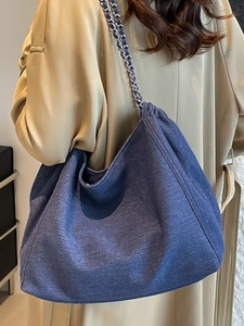 Large capacity dark blue denim tote bag with silver chain strap worn by a model in a trench coat