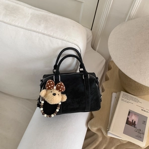 Close-up of black Boston bag on white sofa featuring an embossed logo and cute bear charm