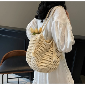 Close-up of cream woven knit bag featuring decorative long tassels and braided shoulder strap